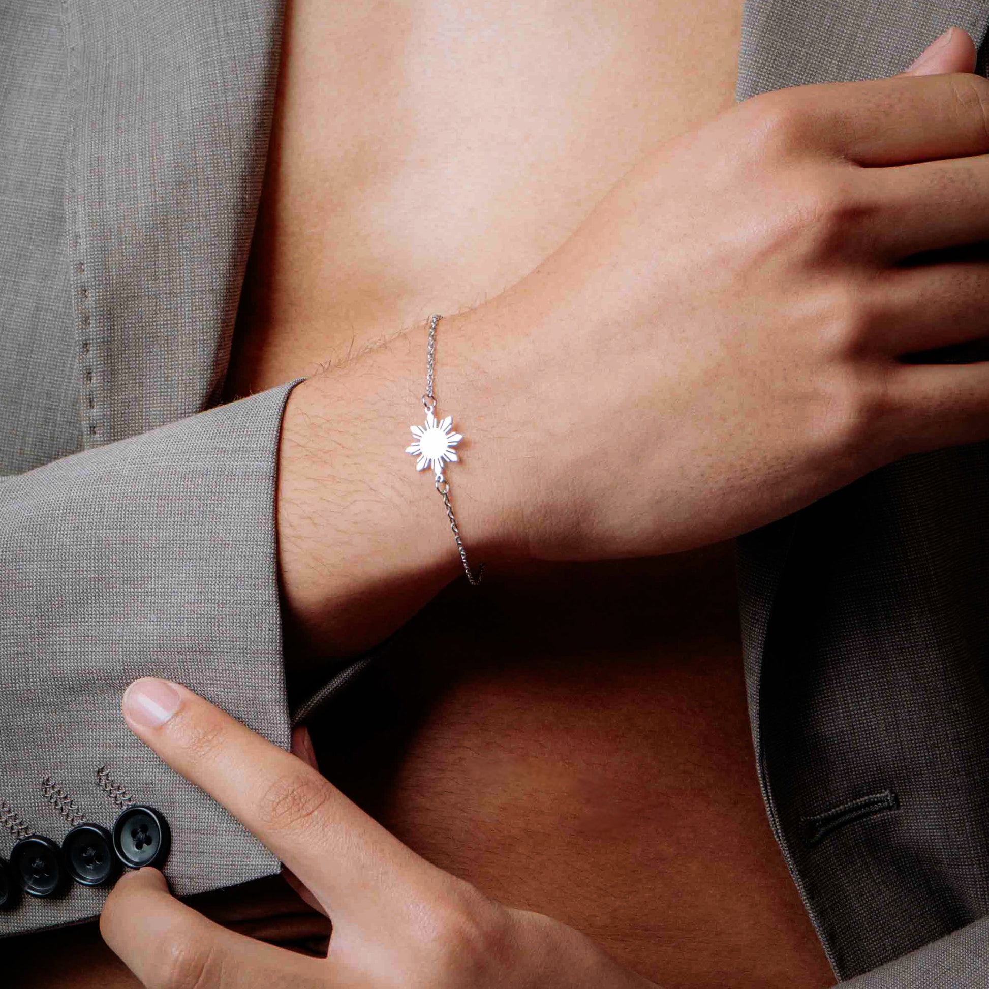 Close up of a man's hand wearing the Araw minimalist silver sun bracelet, featuring a sleek chain and sunburst charm for a modern unisex jewelry look.