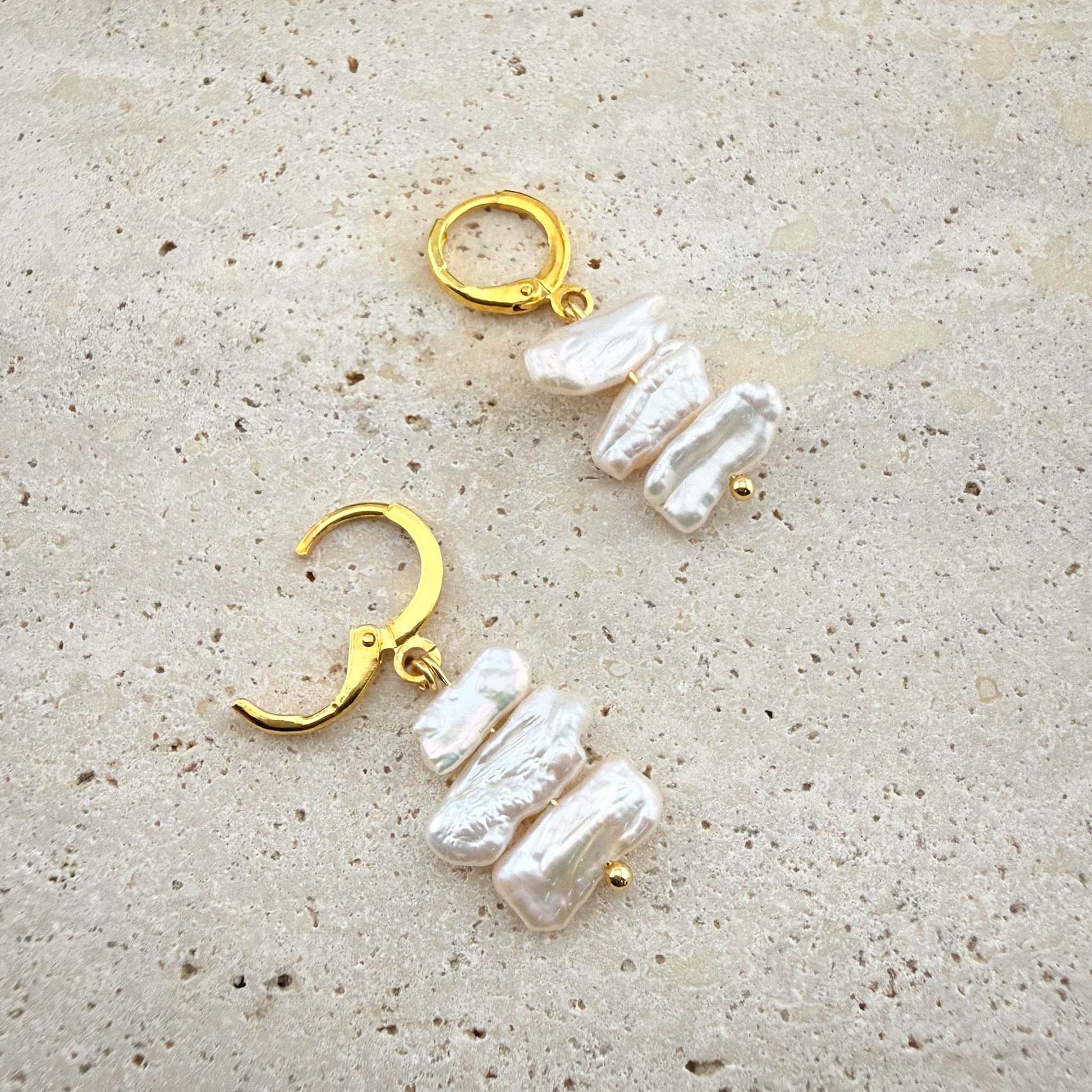 Close-up of gold Triple Flat Keshi Pearl earrings on marble, showing one hoop closed and one with the hinge clasp open to reveal the mechanism.